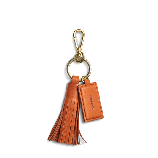 The Leather Tassel Keychain - Rust by Shinola features a gold clasp, large loop, and a rectangular embossed tag—monogrammable for a personalized touch.
