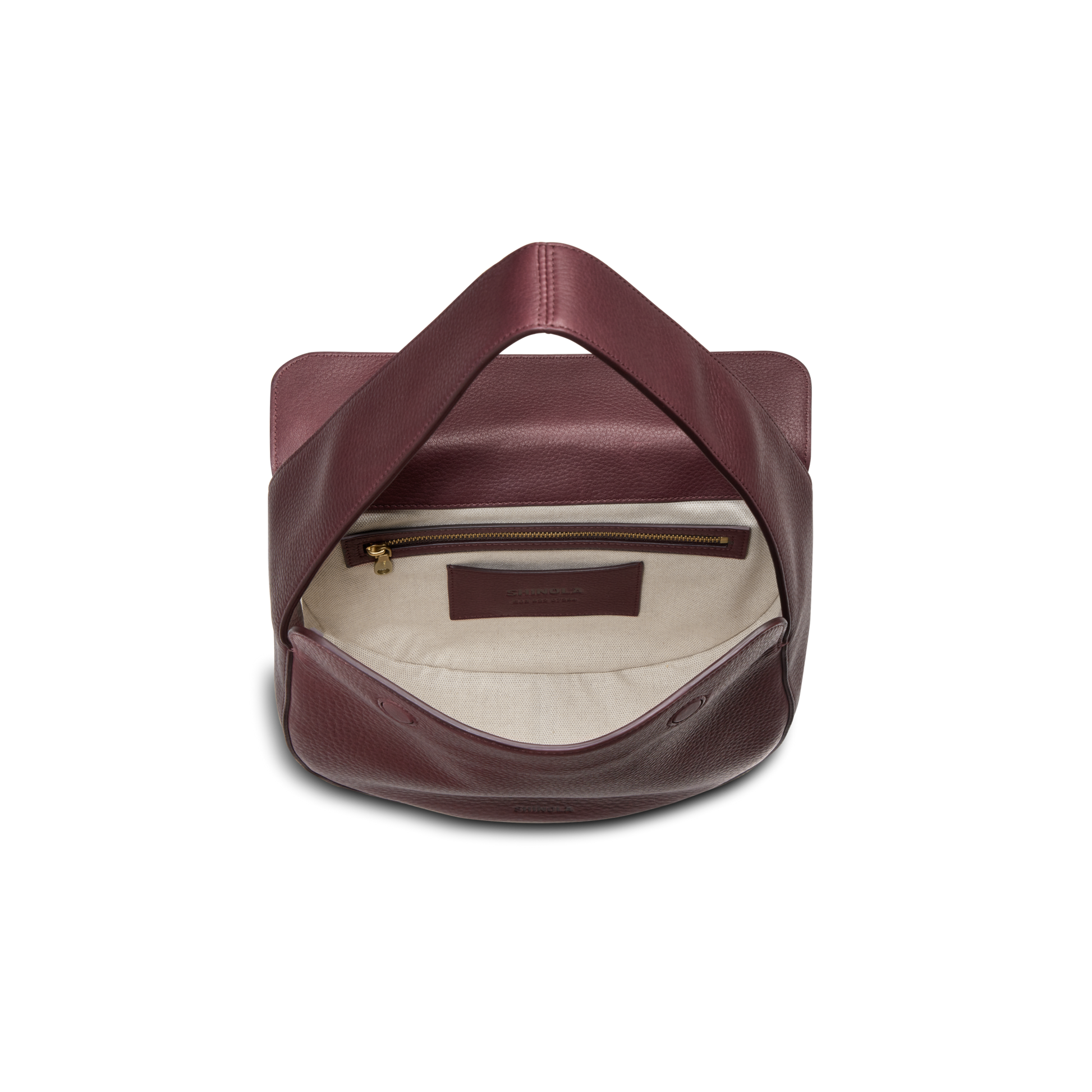 The Shinola Small Shoulder Bag - Merlot is crafted from natural grain leather with a cream interior, a zippered gold pocket, and interior leather logo patch. Its structured design highlights premium craftsmanship and a smooth texture.