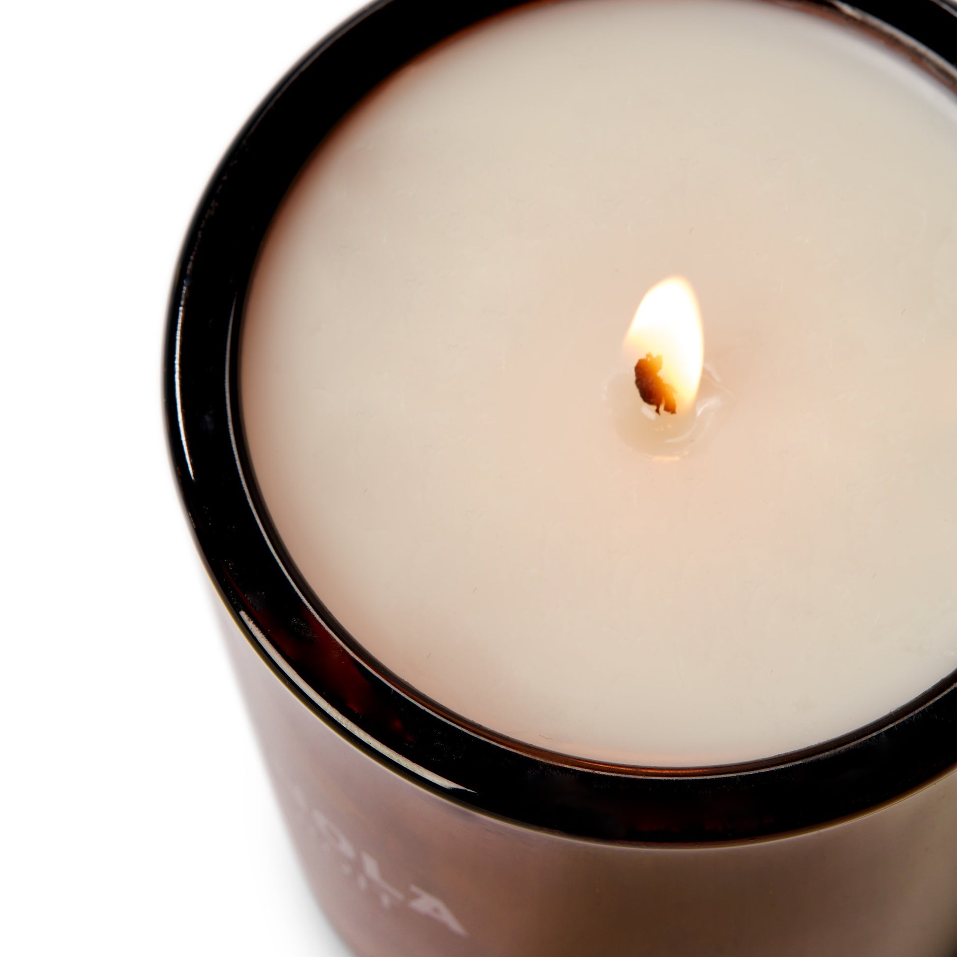 A close-up of the Shinola Hotel 8oz Scented Candle in a recycled glass vessel, featuring coconut soy wax pooling around a small bright flame and partially melted wax visible.