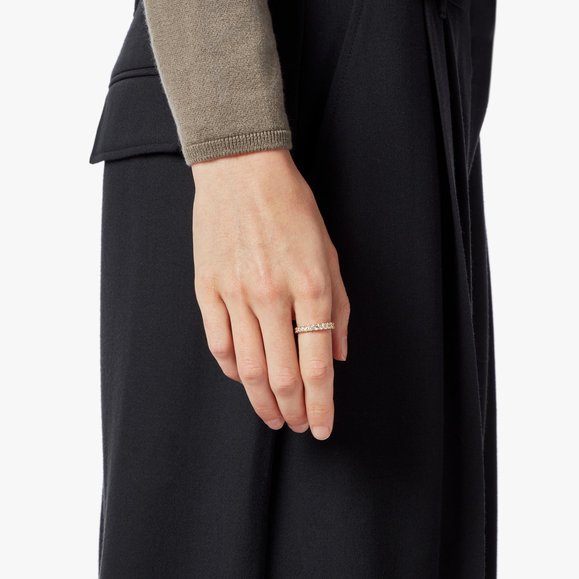 A close-up of a left hand wearing the Shinola 1 Carat Diamond Anniversary Band in yellow gold, shown against a black skirt or pants and a taupe long-sleeve top. The relaxed hand rests at the person's side.