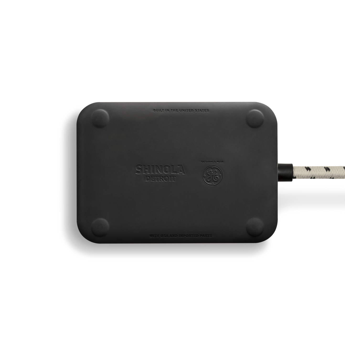 A black rectangular 5 Port Power Supply - Stone by Shinola, with rounded corners, a braided cord on the right, and “Built in the United States” embossed on it.