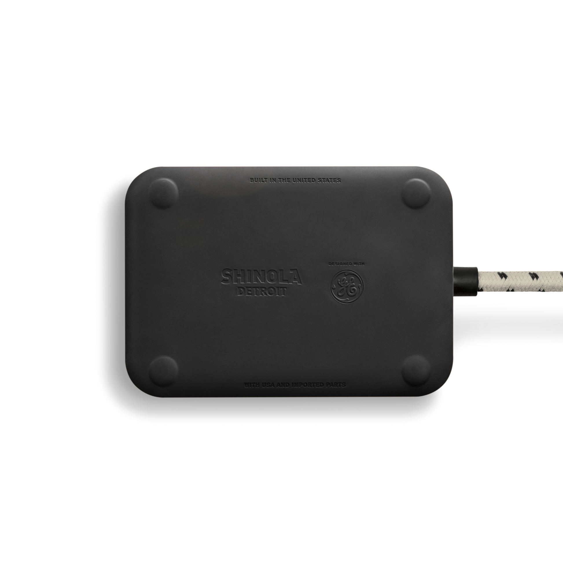 A black rectangular 5 Port Power Supply - Stone by Shinola, with rounded corners, a braided cord on the right, and “Built in the United States” embossed on it.