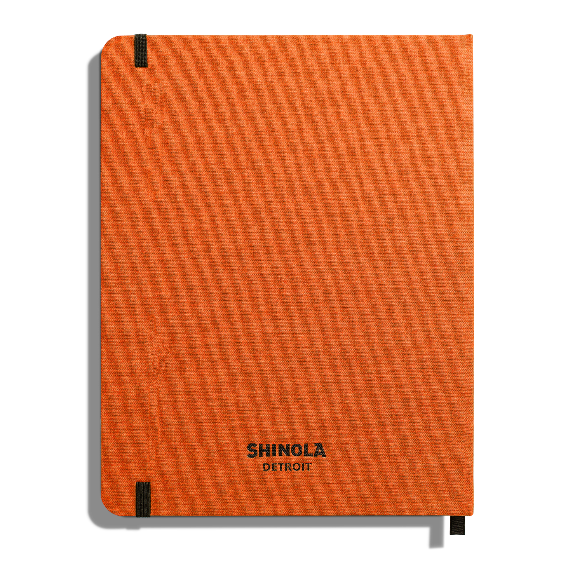 The Shinola Large Hard Ruled Journal in Bold Orange features a hard linen cover, smyth-sewn binding, black corner elastic bands, and “Shinola Detroit” printed in black near the bottom center of the cover.