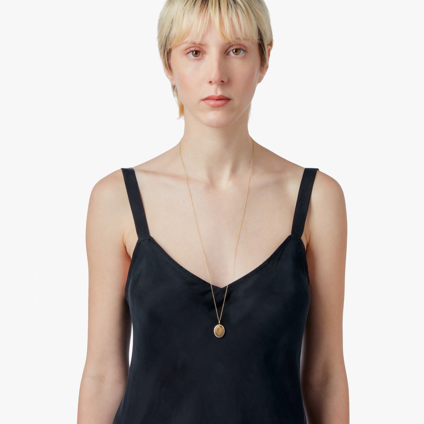 A person with short blonde hair, in a black sleeveless top and a long Shinola Diamond Pave Petoskey Necklace in yellow gold, stands against a plain white background.