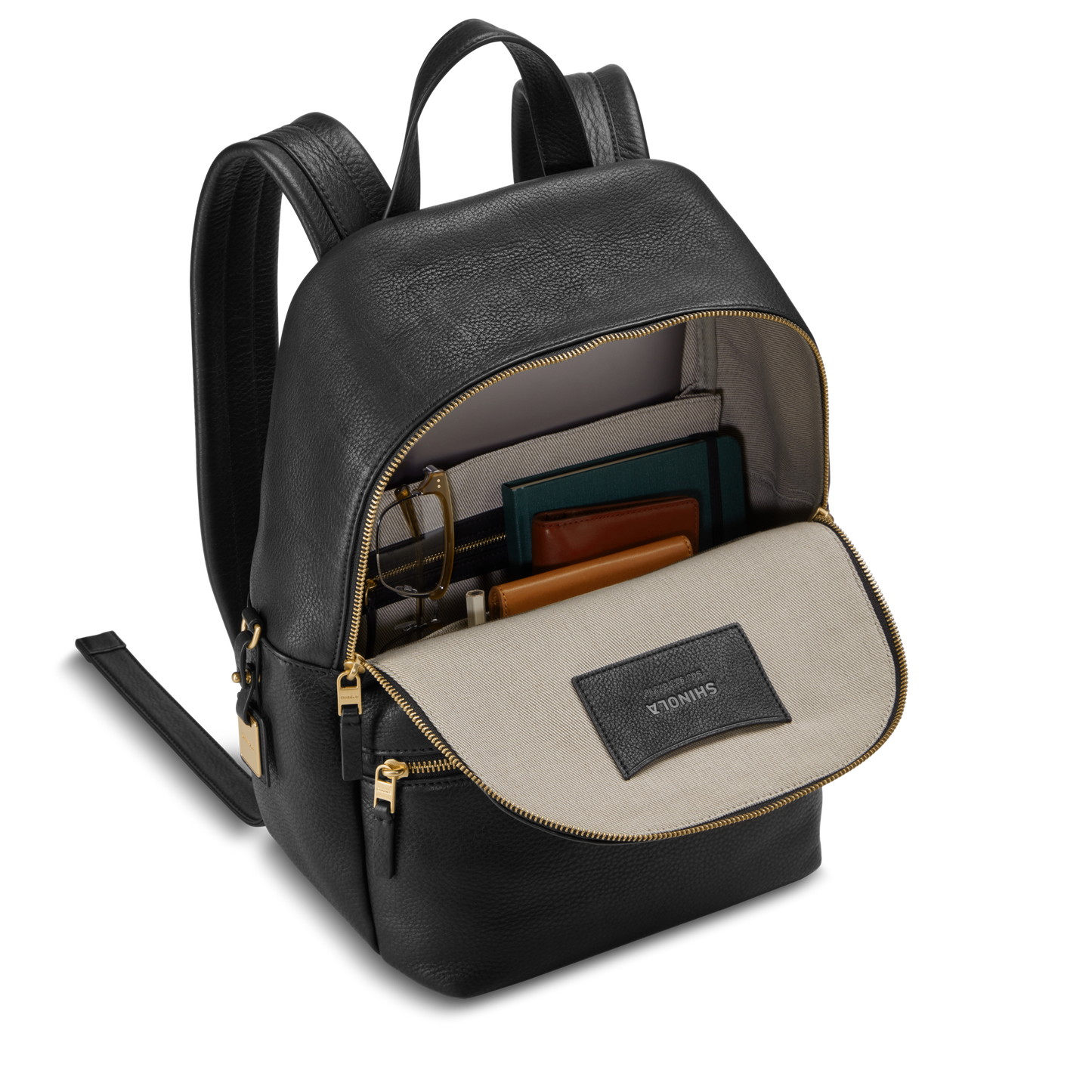 The Shinola Small Runwell Backpack in black is open, revealing a beige interior with a branded label and gold zippers. Inside, notebooks, a folder, glasses, and a wallet are neatly organized and securely held.