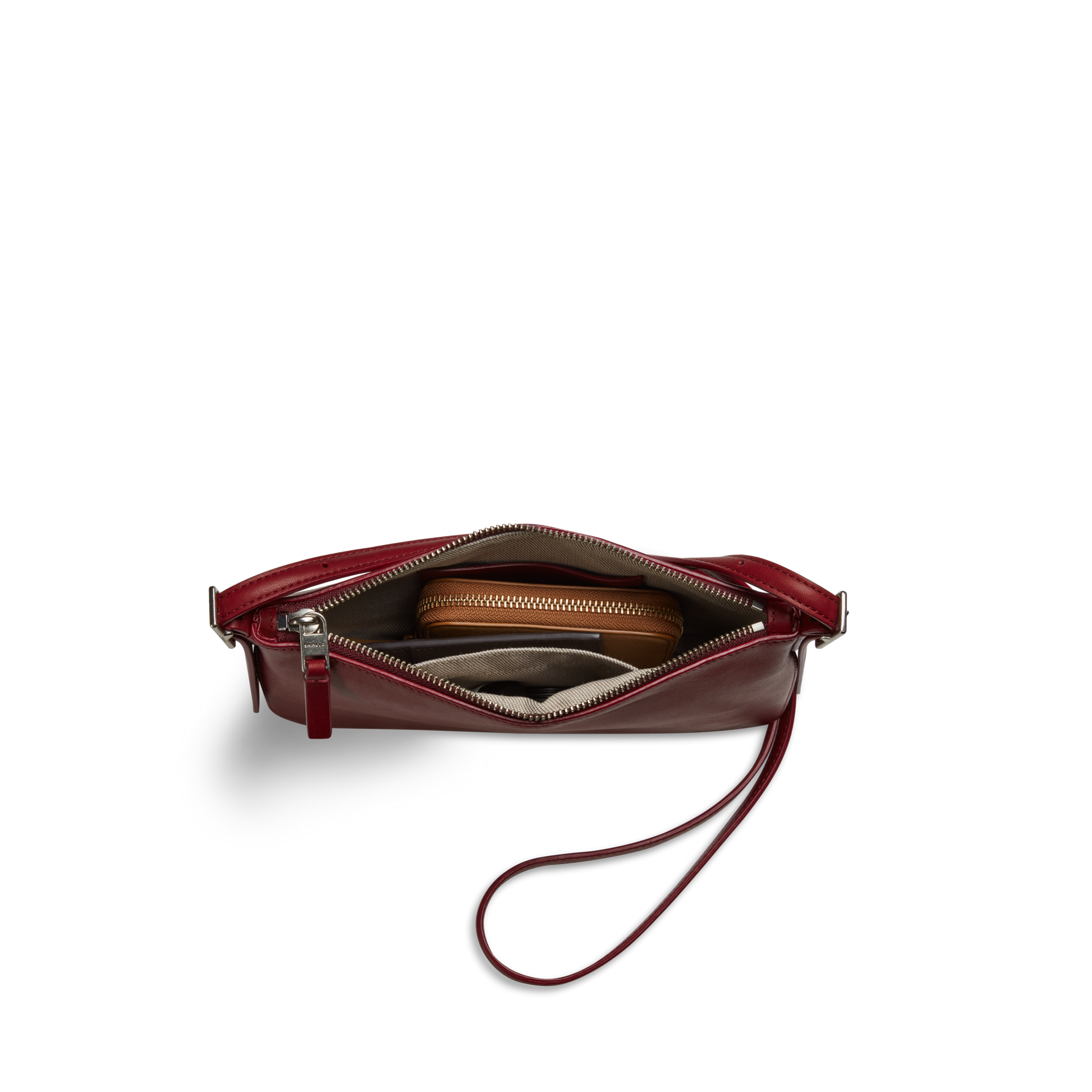 The Shinola Small Bixby Crossbody in Ruby is a compact maroon leather wristlet, shown from above with the zipper open to reveal a brown wallet and other small items—an everyday accessory for convenience.
