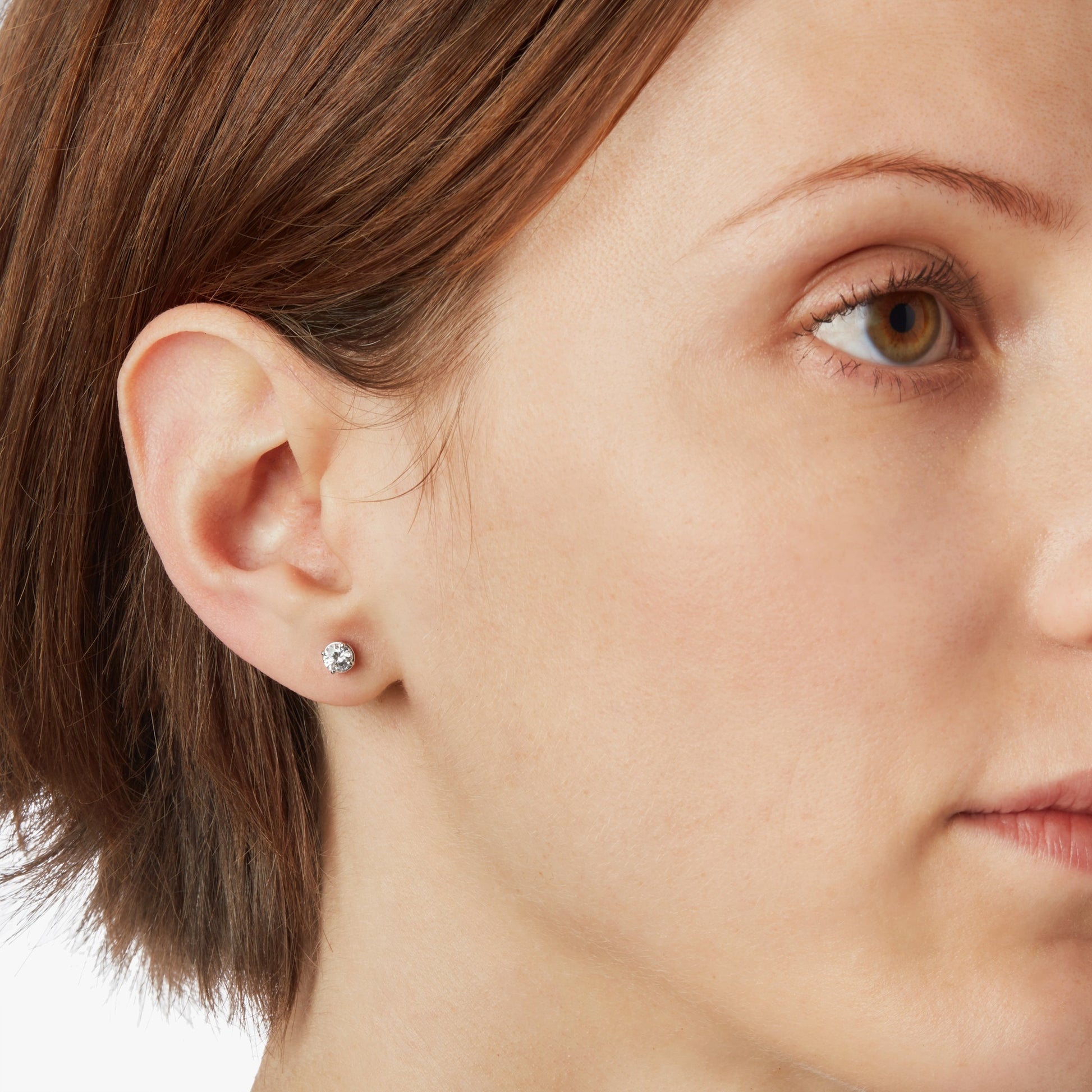 Close-up of a woman with light skin and short brown hair wearing Shinola 1 Carat Round Diamond Studs in white gold, highlighting the classic diamond earring.