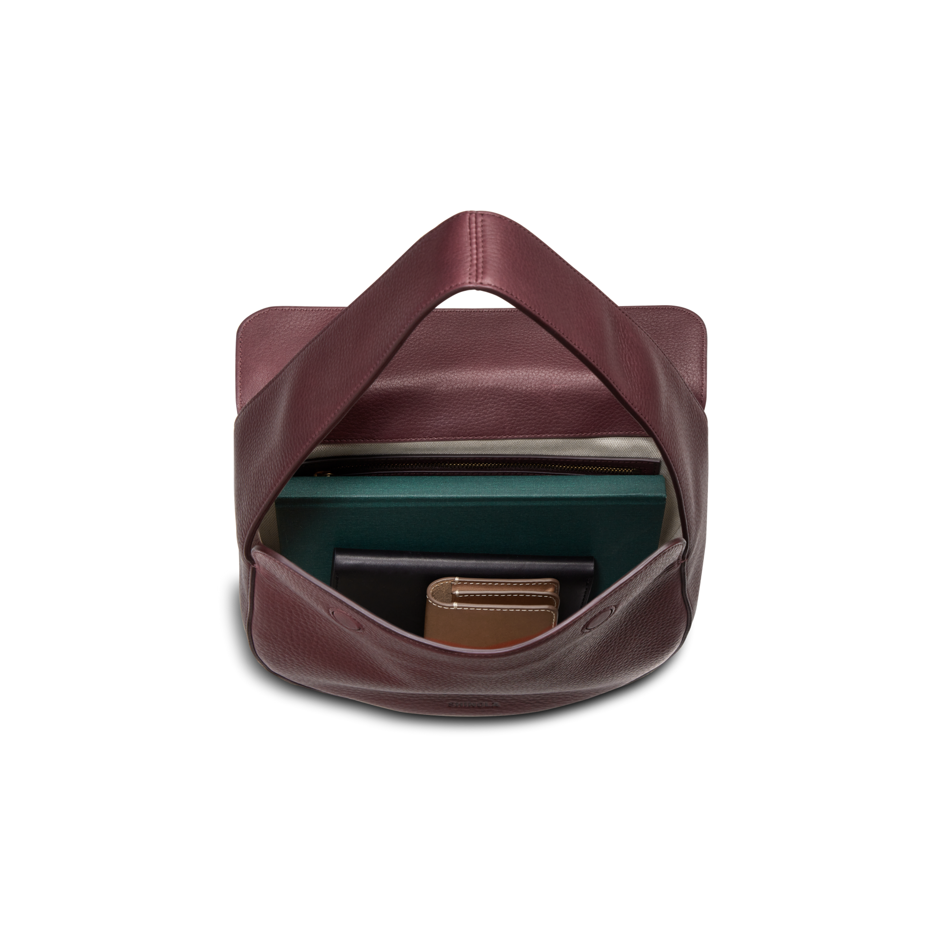 A Shinola Small Shoulder Bag - Merlot in natural grain leather is shown with its flap open, neatly holding a green notebook, brown wallet, and a small dark item inside, all set against a white background.