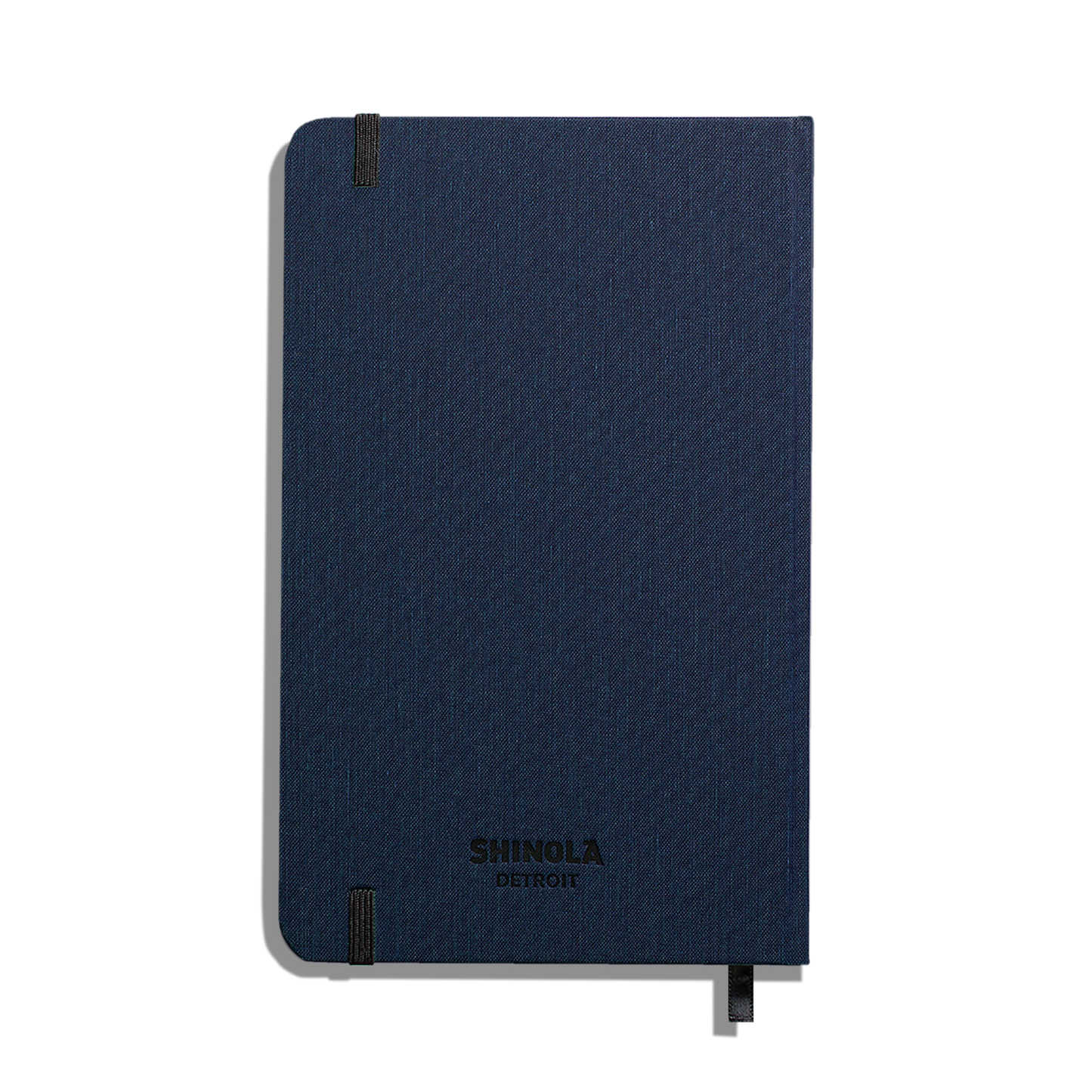 A closed, navy Medium Hard Ruled Journal by Shinola with black elastic bands on two corners. SHINOLA DETROIT is printed in black near the bottom center—ideal for fans of linen journals and acid-free paper.