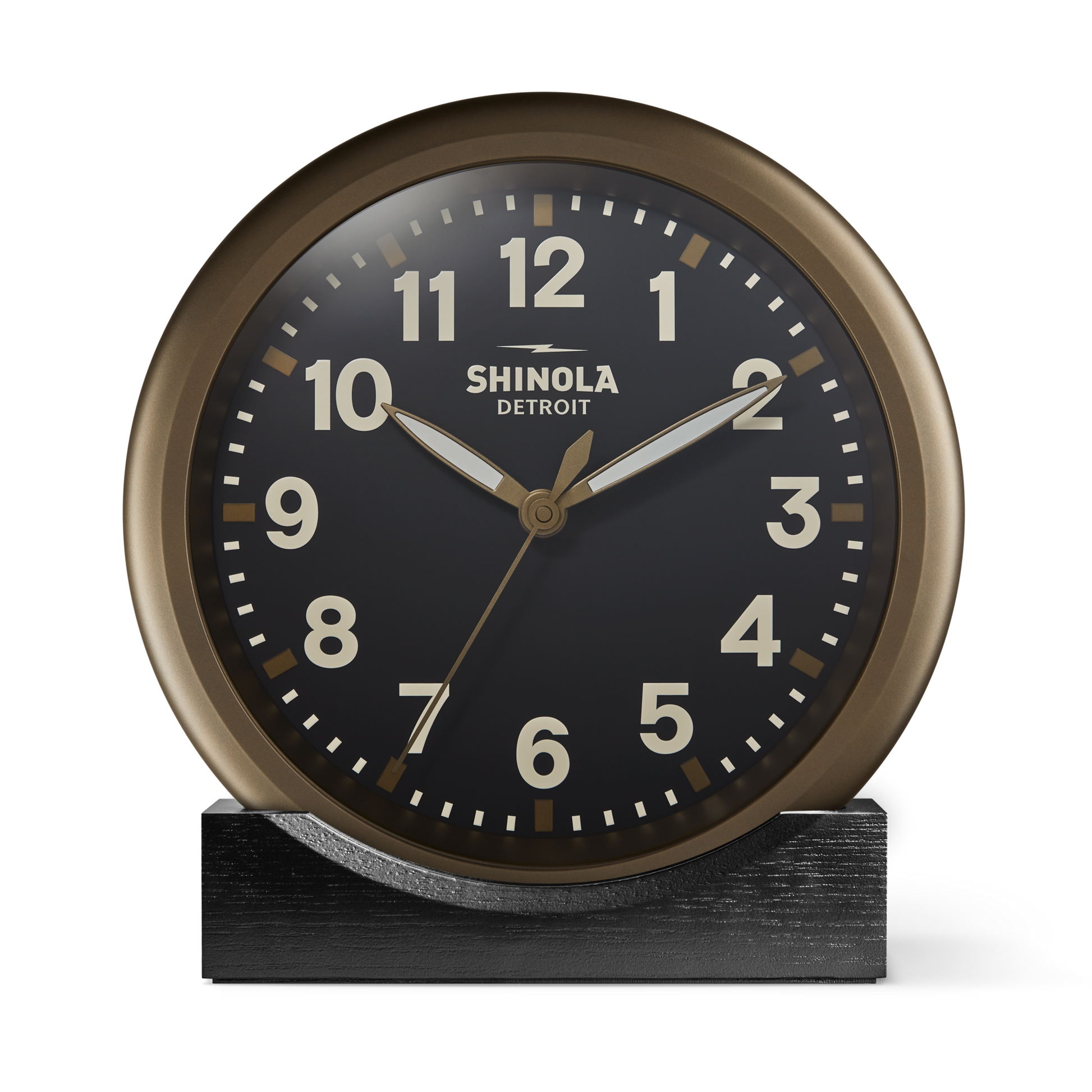 The 14" Runwell Clock by Shinola features a round, vintage-inspired design with a black face, white numerals, and gold hands. It sits on a black rectangular base, reads 10:10, and displays 'Shinola Detroit' on the face.