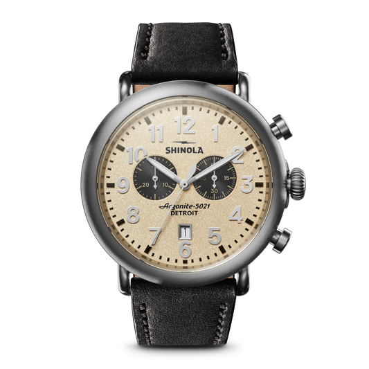 The Shinola Runwell Chronograph - Cream features a beige dial, black subdials, stainless steel case, black leather strap, Arabic numerals, two chronograph dials, and prominent pushers on the right.