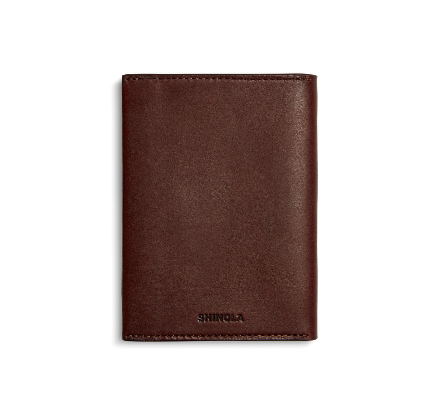 A closed, merlot Shinola Passport Holder made from Italian Vachetta leather stands upright on a white background. SHINOLA is embossed at the bottom center, highlighting its refined appeal as a travel accessory.