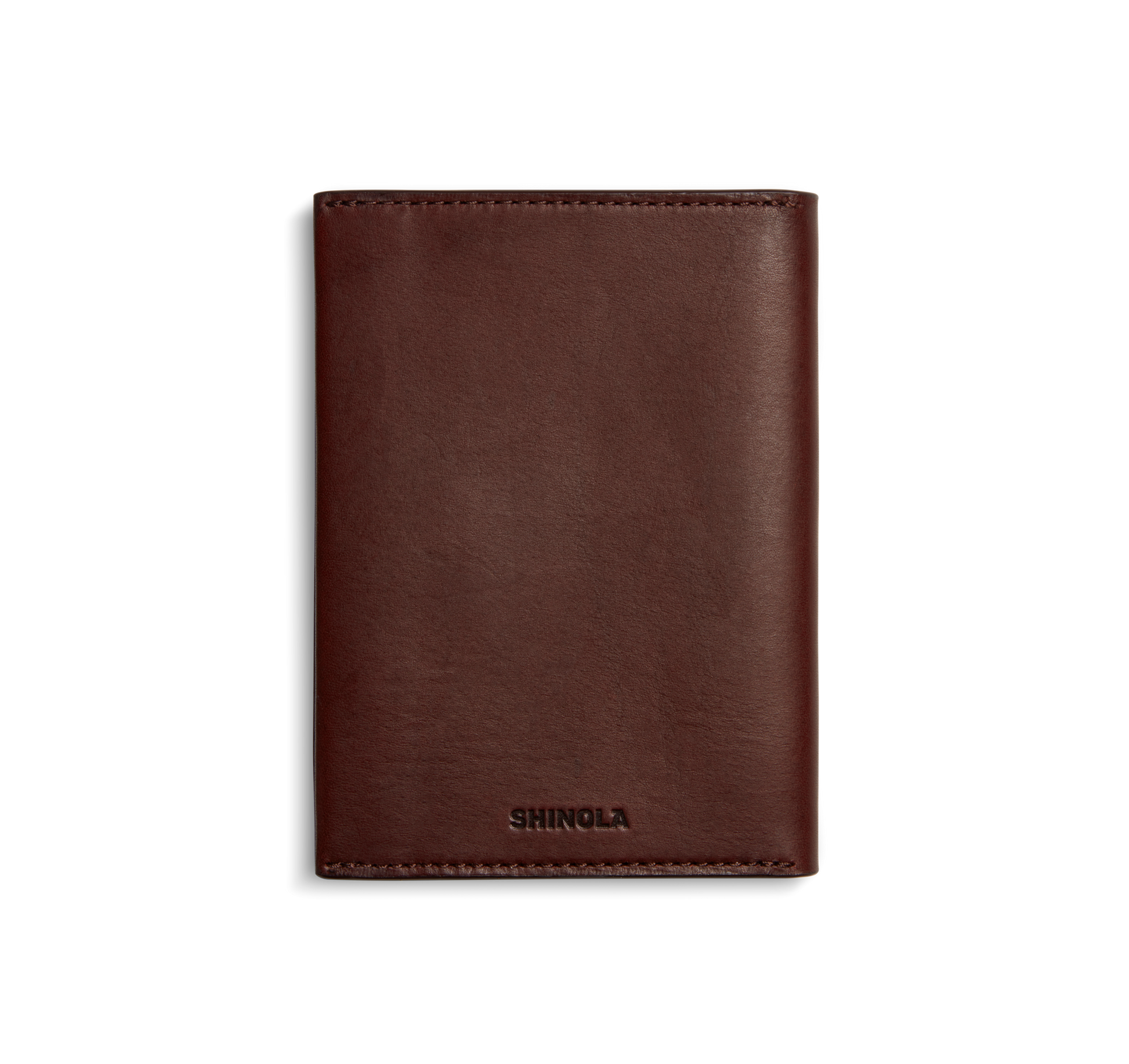A closed, merlot Shinola Passport Holder made from Italian Vachetta leather stands upright on a white background. SHINOLA is embossed at the bottom center, highlighting its refined appeal as a travel accessory.