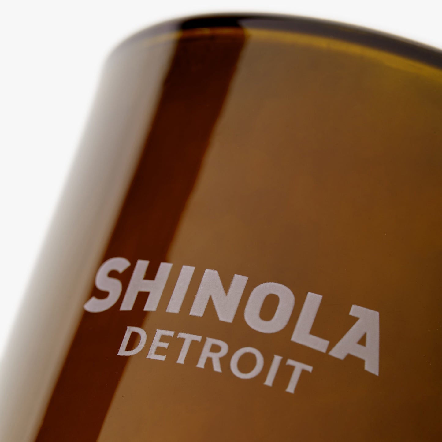 Close-up of a Shinola Hotel 8oz Scented Candle with "SHINOLA DETROIT" printed in white on the brown recycled glass vessel.