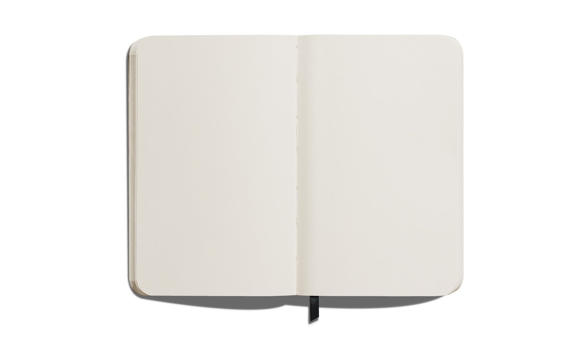 The Shinola Medium Hard Plain Journal in Navy features cream-colored pages, rounded corners, and lies flat on a white surface. A black ribbon bookmark is visible at the bottom center.