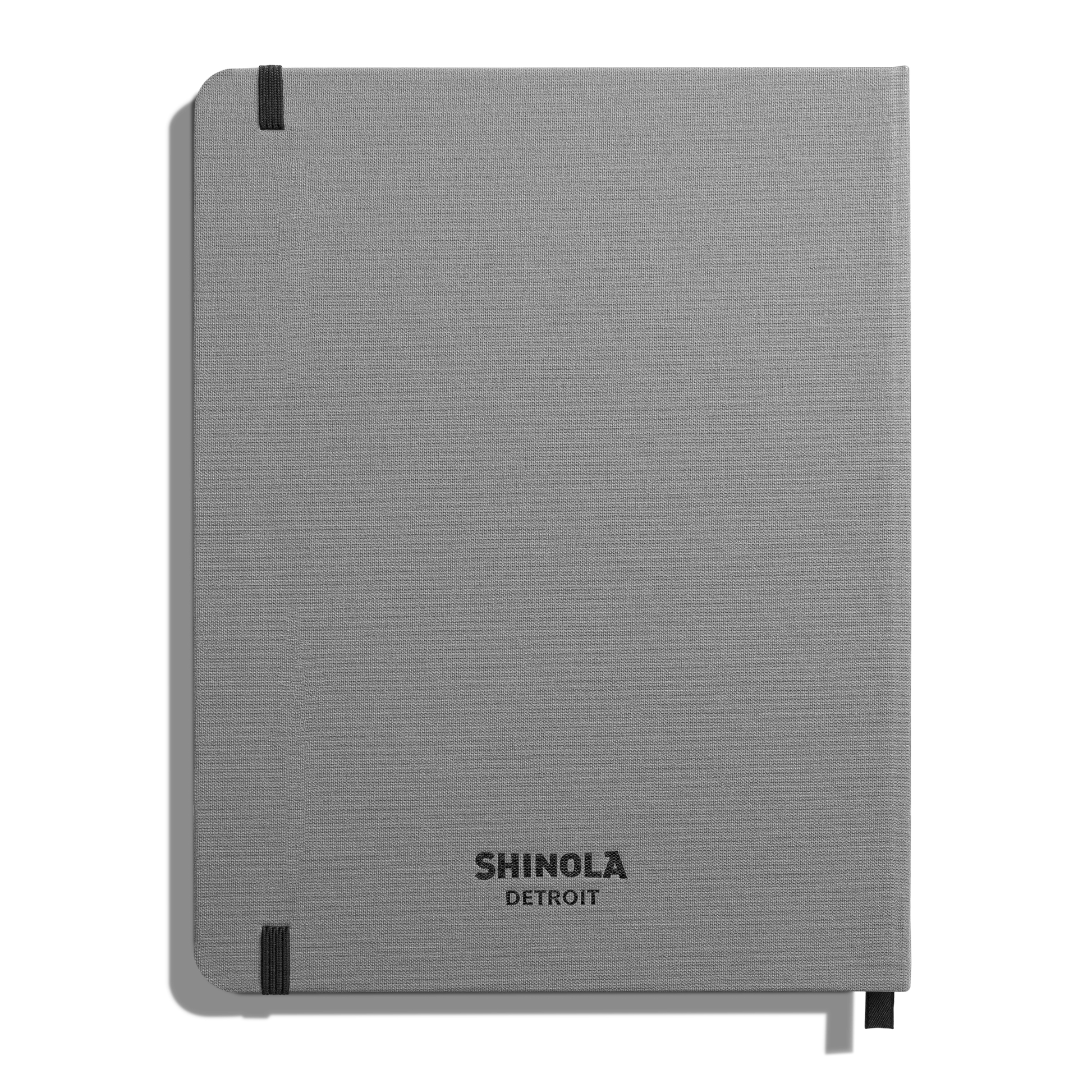 The Large Hard Grid Journal - Stone by Shinola is a closed, light gray hardcover notebook with smyth-sewn binding and black elastic bands on two corners. "SHINOLA DETROIT" is printed in black near the bottom of the cover.