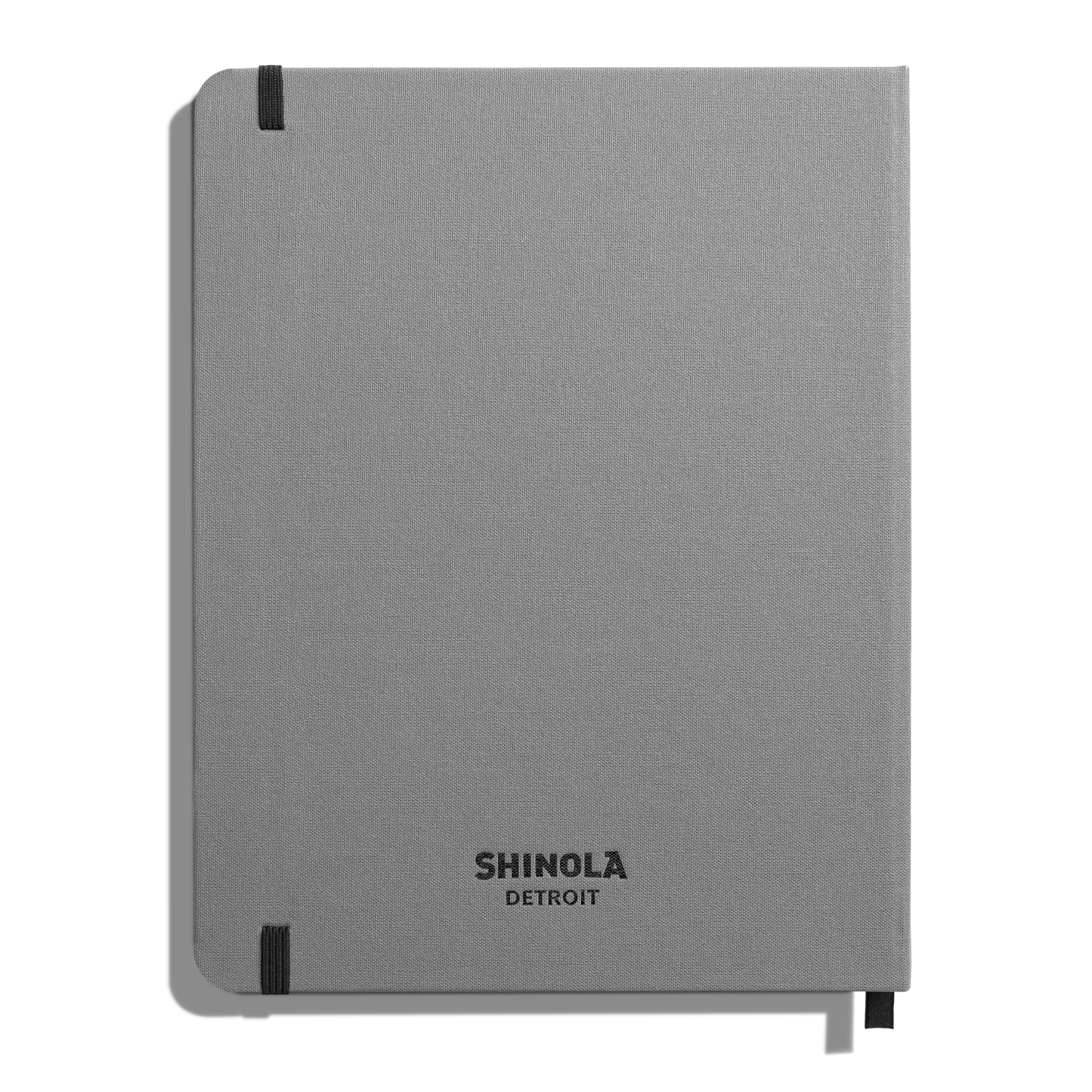 The Shinola Large Hard Ruled Journal - Stone is a gray hardcover notebook with smyth-sewn binding, black elastic bands on two corners, and "SHINOLA DETROIT" printed in black on the front cover.