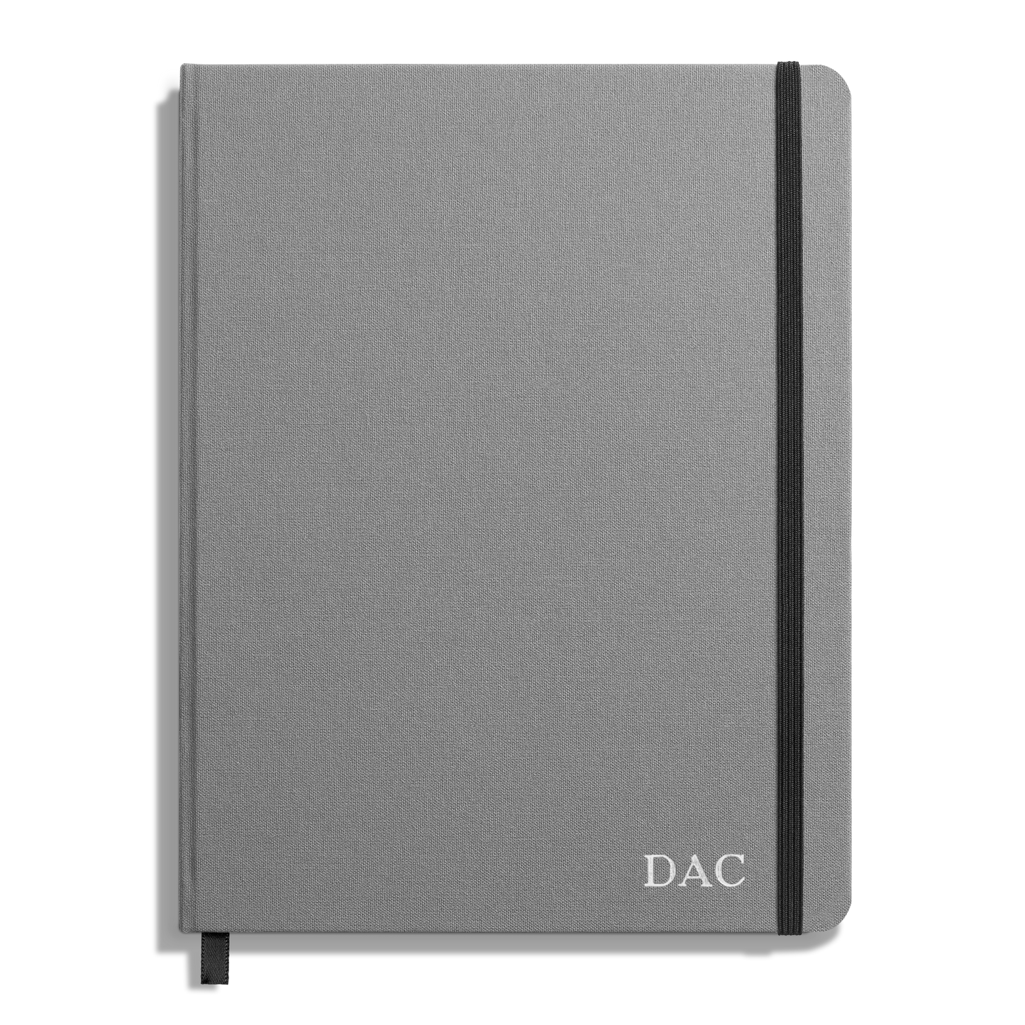 The Shinola Large Hard Plain Journal - Stone is a closed, gray hardcover with a black elastic band, a black ribbon bookmark, and DAC initials in white on the bottom right corner—crafted with durable acid-free paper.
