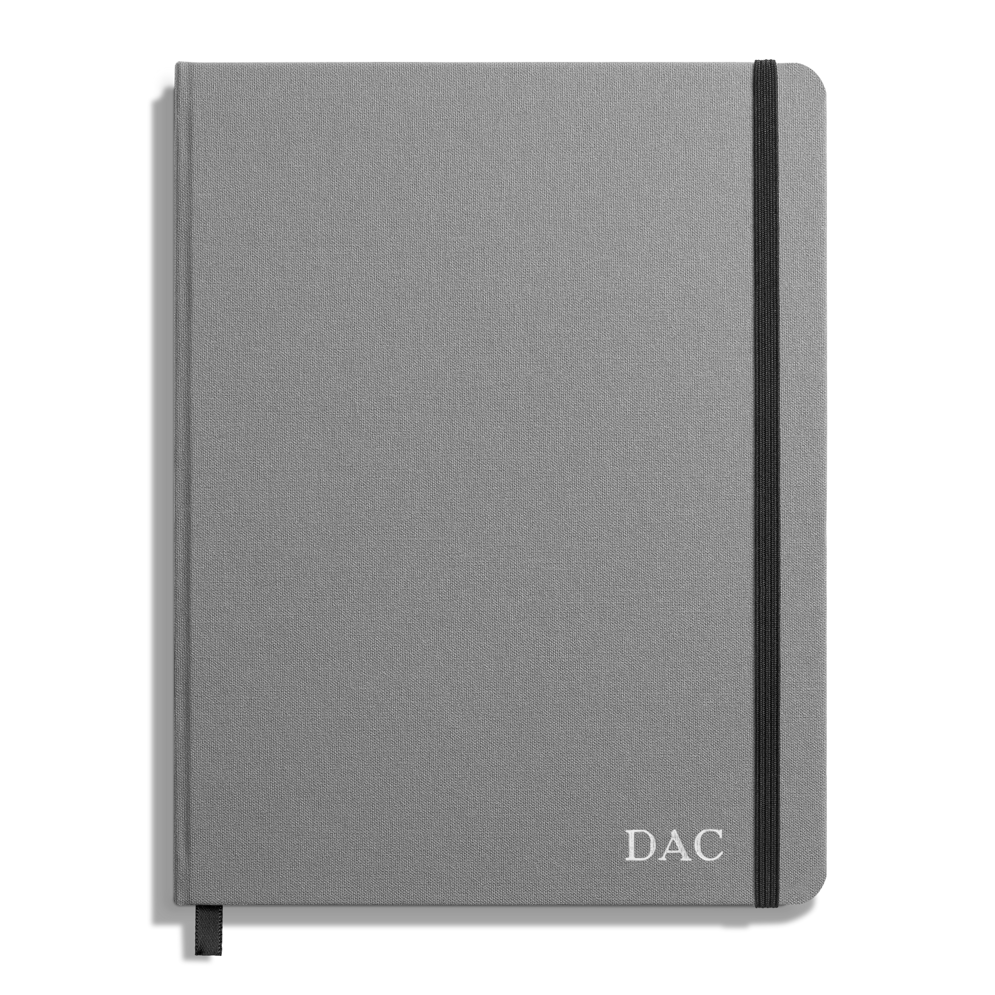 The Shinola Large Hard Plain Journal - Stone is a closed, gray hardcover with a black elastic band, a black ribbon bookmark, and DAC initials in white on the bottom right corner—crafted with durable acid-free paper.