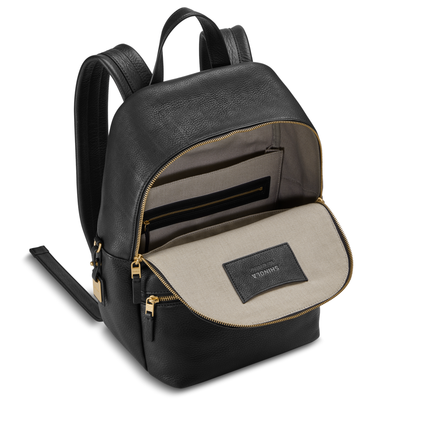 The Small Runwell Backpack by Shinola is shown open in black natural grain leather with gold zippers, revealing a beige fabric interior with a zip pocket and a stitched SHINOLA label.