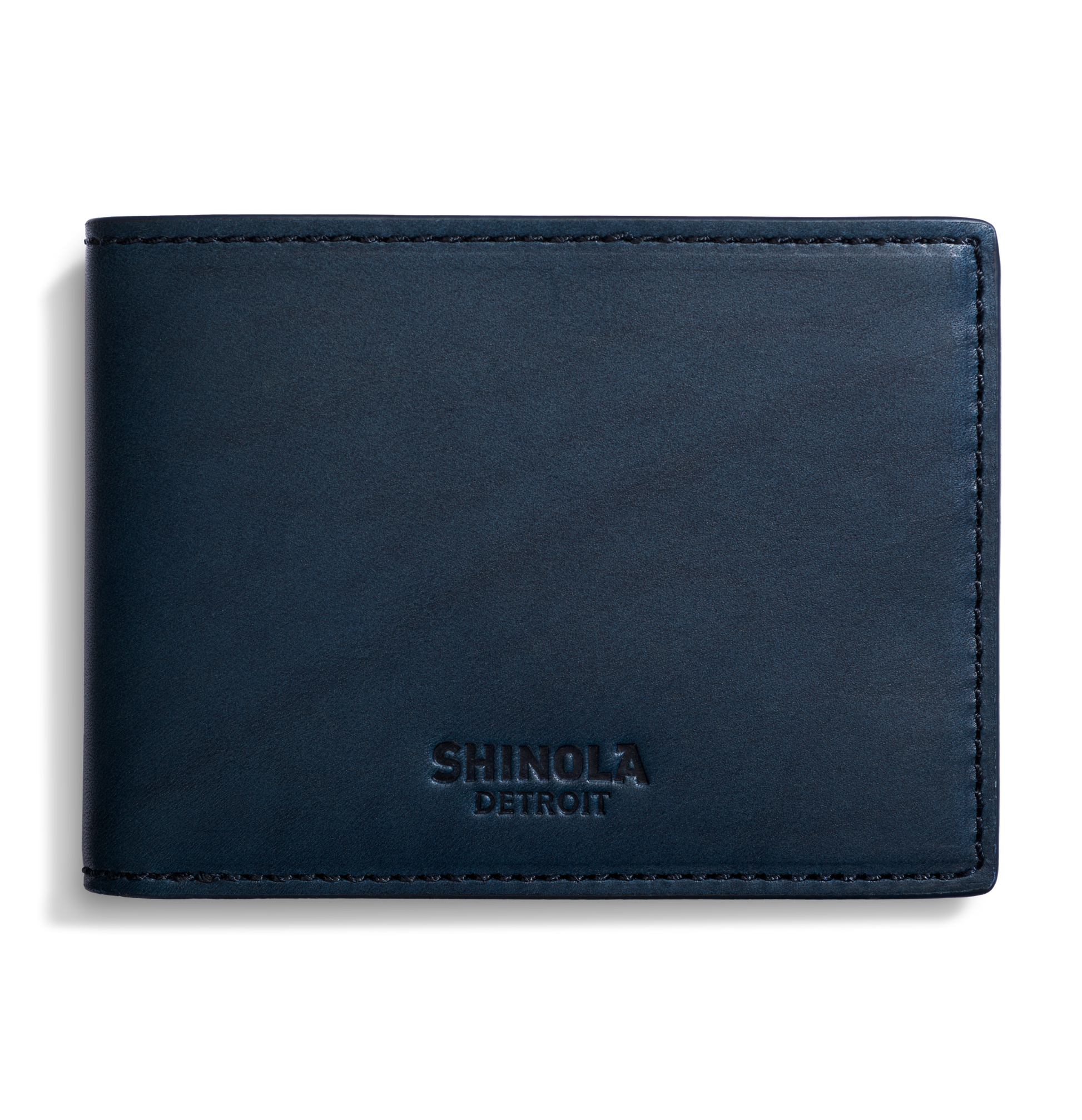 A closed Slim Bifold Wallet in navy leather by Shinola, featuring embossed branding on the lower front, displayed against a plain white background.