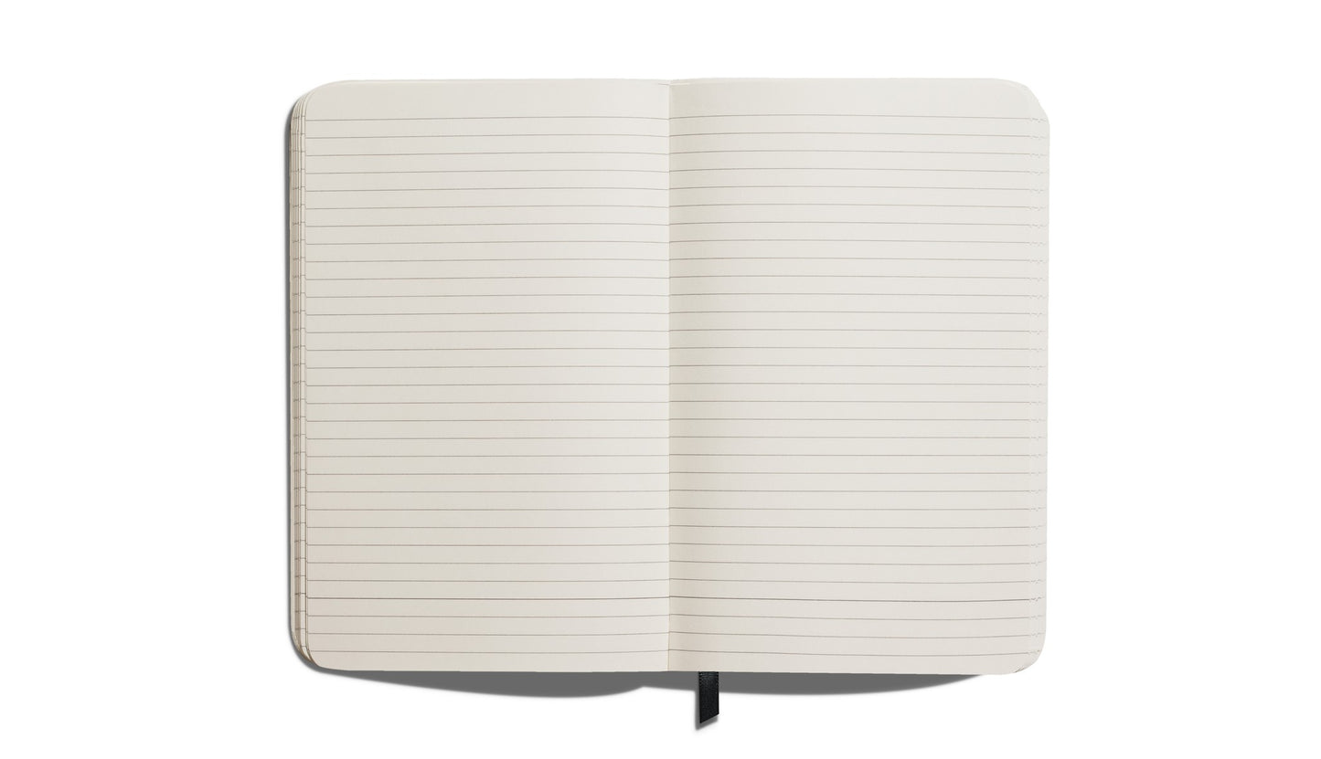 The Shinola Medium Hard Ruled Journal in Bold Orange—crafted in America with acid-free paper—features lined pages, a black ribbon bookmark, and is shown open from above on a white background.